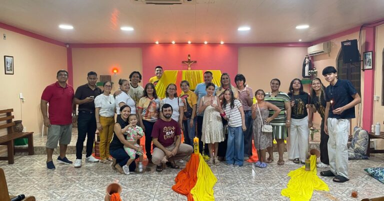 Jovens, adultos e famílias posam para foto ao final do Lucernário em honra a Santa Rosa de Lima, realizado em espaço comunitário decorado com velas e elementos religiosos.