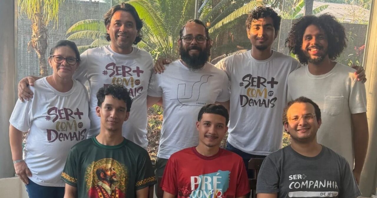 Grupo de oito participantes do GAVI posa para foto, com cinco pessoas em pé e três sentadas, em ambiente iluminado e com vegetação ao fundo.