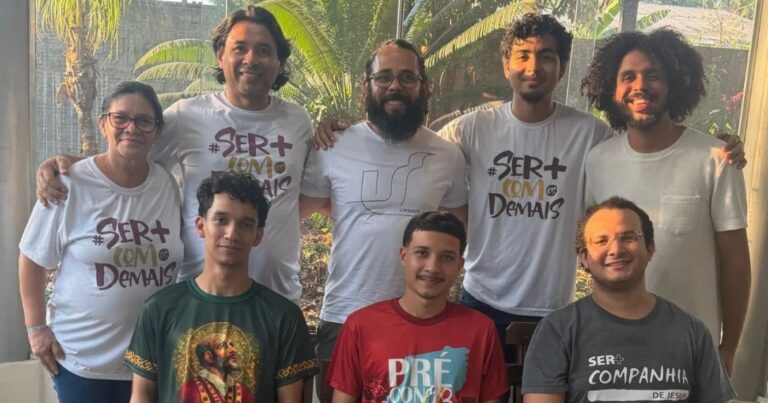 Grupo de oito participantes do GAVI posa para foto, com cinco pessoas em pé e três sentadas, em ambiente iluminado e com vegetação ao fundo.