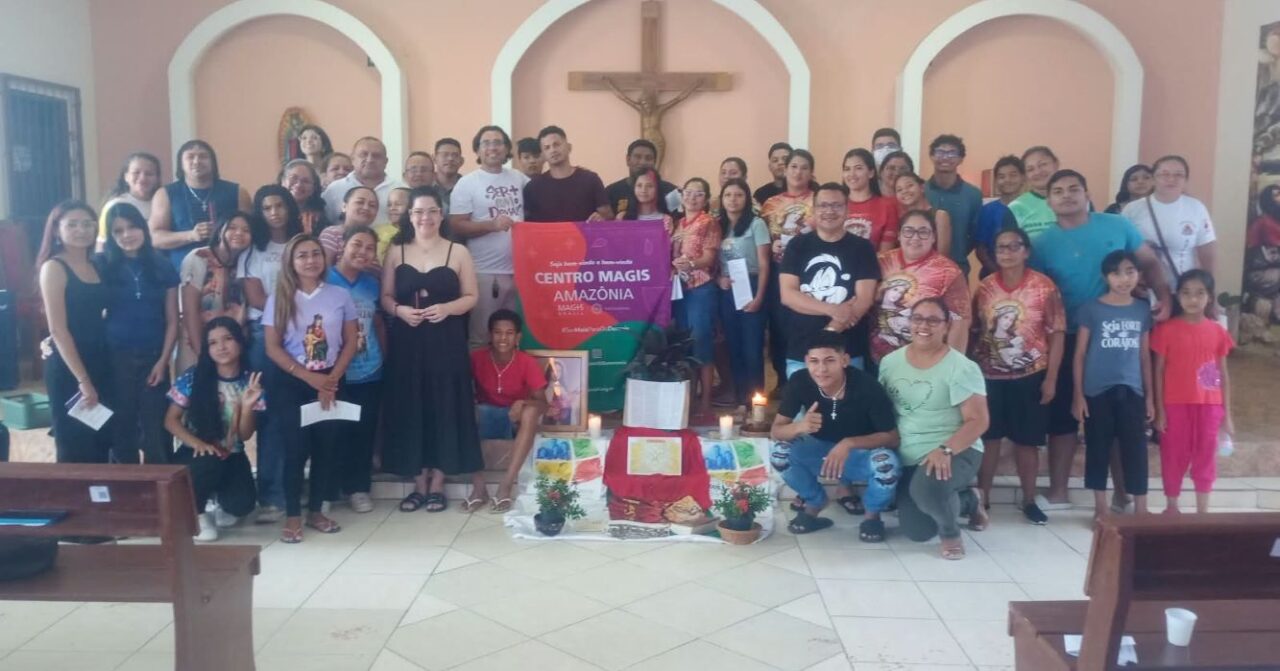 Participantes do retiro de preparação para a Crisma posam para foto em uma igreja, junto à bandeira do Centro MAGIS Amazônia, diante do altar e de um crucifixo.