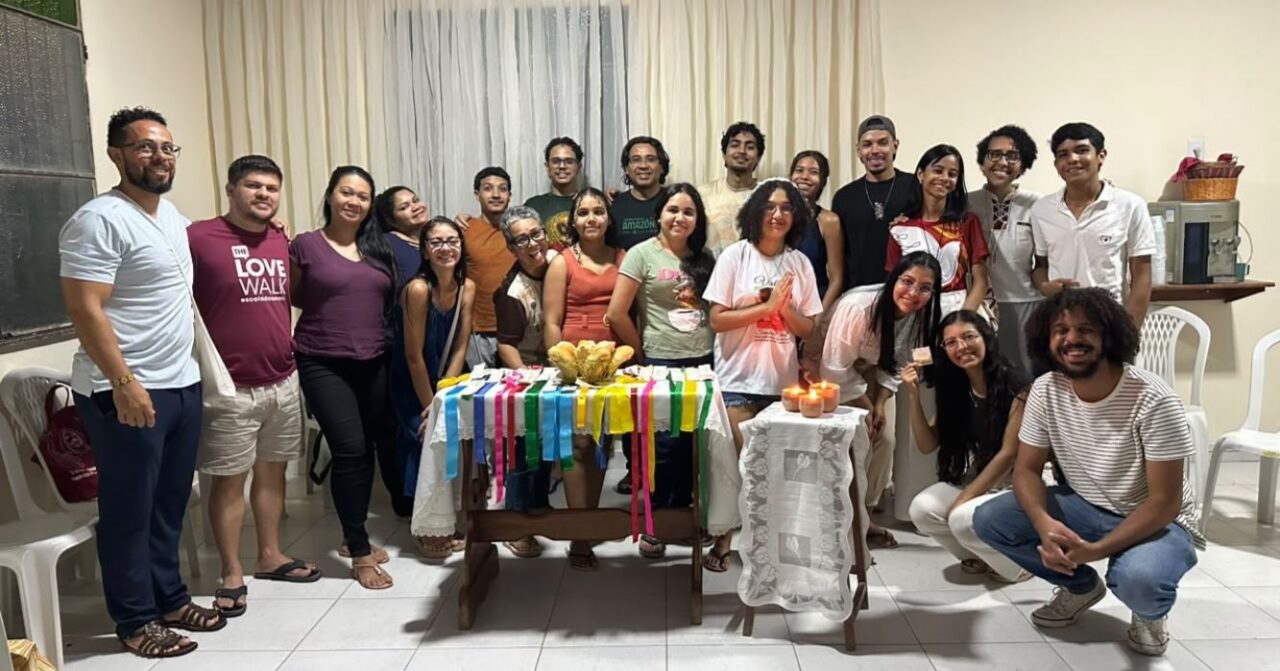 Participantes dos encontros vocacionais “A mesa ainda está posta”, realizados em Manaus (AM), reunidos ao redor de uma mesa decorada com fitas coloridas, alimentos e velas, em um momento de convivência e partilha.
