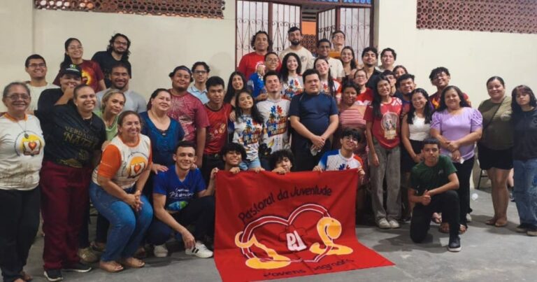 Participantes da Noite da Lasanha promovida pelo grupo Jovens Sagrados, da Pastoral da Juventude, em Manaus (AM), reunidos em foto coletiva com a bandeira da PJ durante a mobilização para a apresentação “O Verdadeiro Natal”.